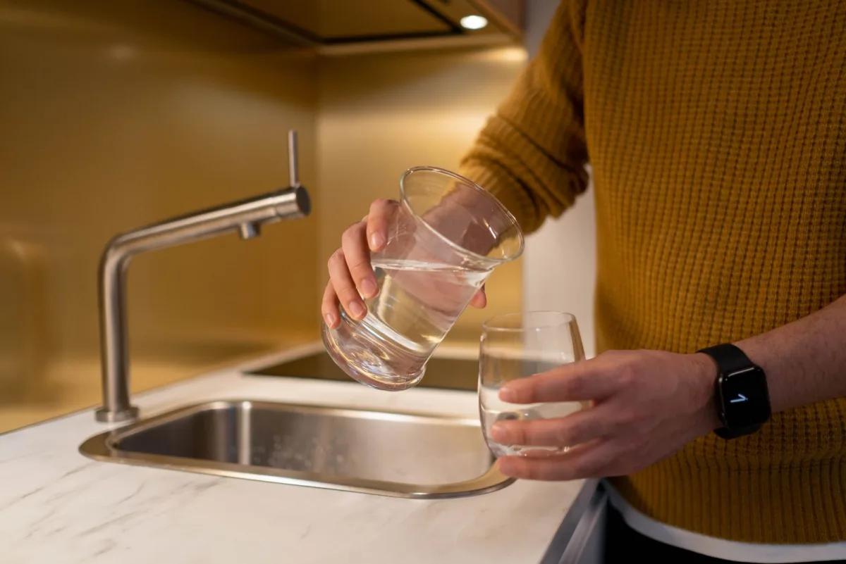 A person filling a clear drinking glass with water in a warm, softly lit home kitchen