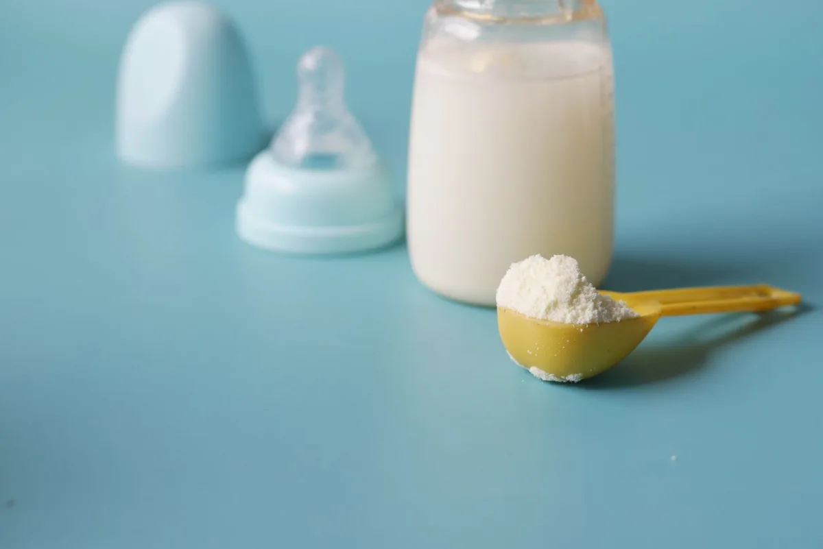 A scoop of infant formula powder beside a baby bottle, ready for mixing with clean water