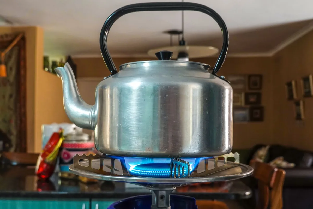 A stainless steel kettle heating on a gas stovetop in a cozy warm kitchen