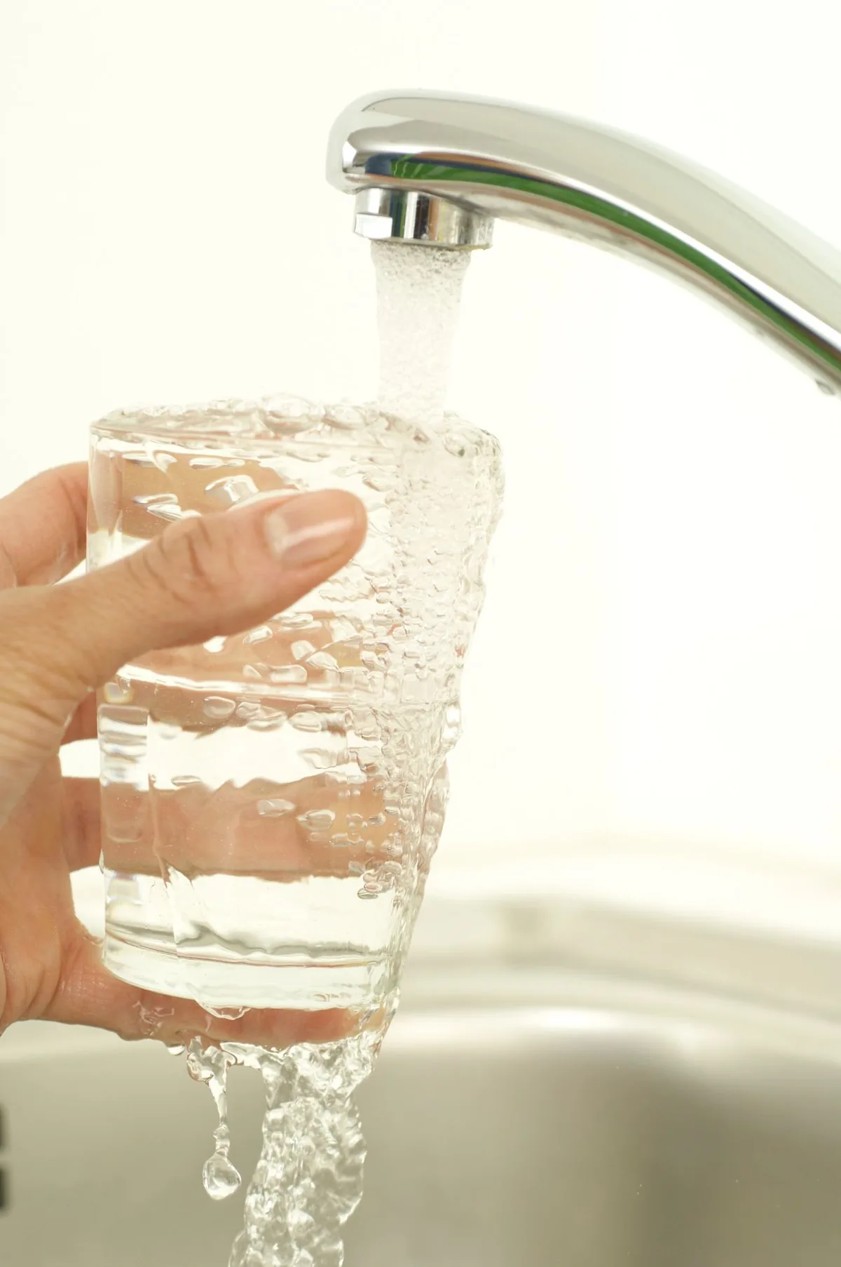 Hand filling a clear glass with tap water