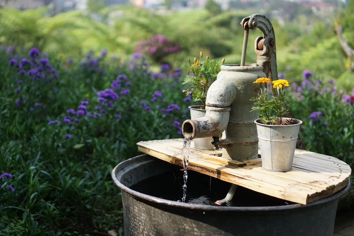 Rural gray deep well pump among garden flowers