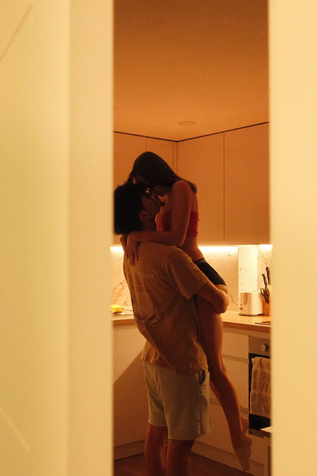 A couple embracing warmly in a cozy, softly lit home kitchen