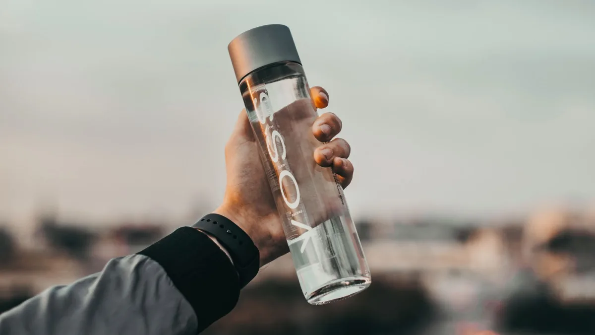 A hand holding a clear glass vessel of water like a collected sample in daylight